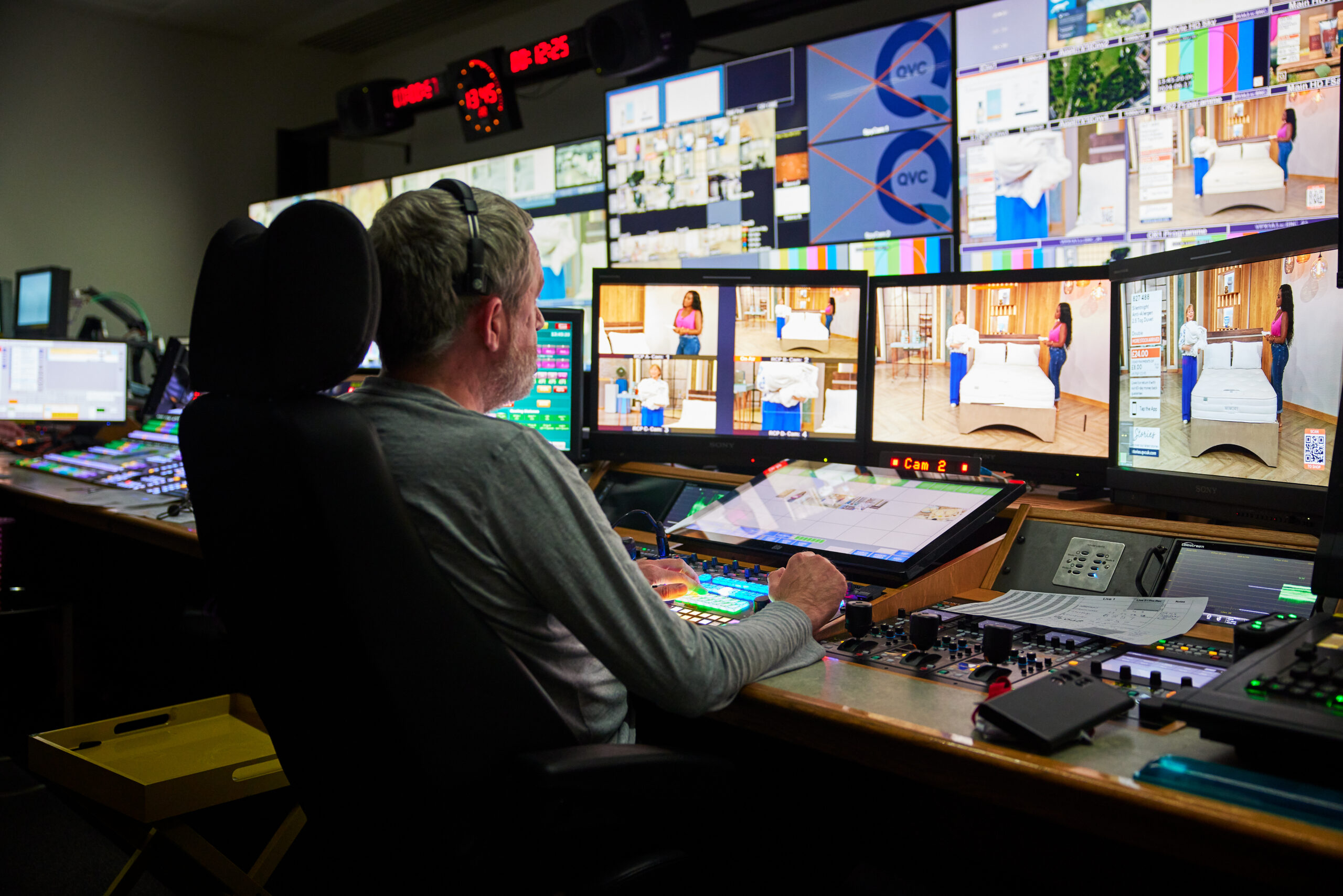 A QVC UK producer in front of multiple screens in the board room focusing on operating the live QVC show.