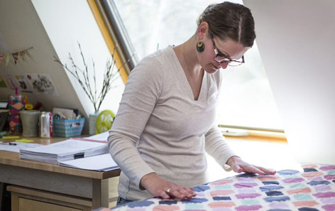 A woman with glasses looking down at patterns on a quilt.