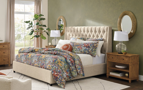 A cozy bedroom set featuring a floral patterned comforter and comfortable rug. There are wooden side tables in frame.